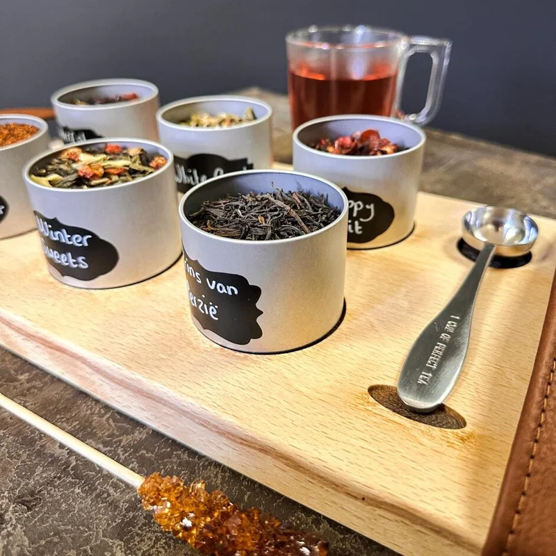 Losse thee in blikjes met een glas verse thee op een houten plank